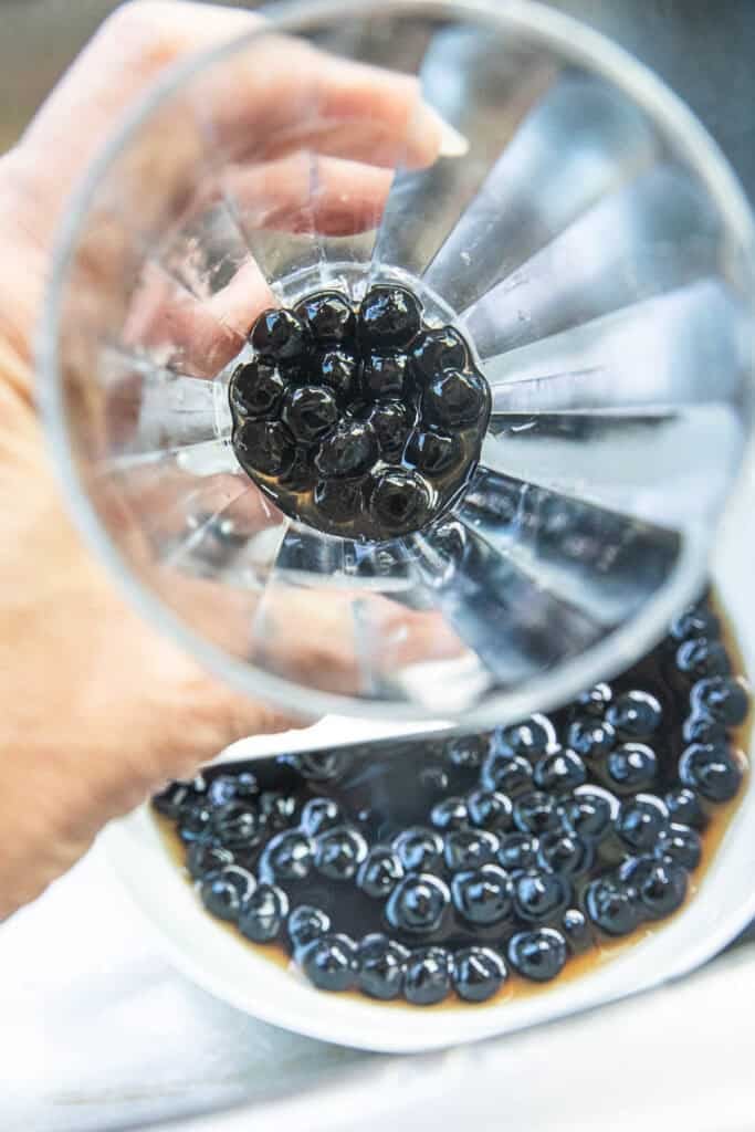 Homemade black boba pearls in a glass over a bowl of more boba pearls. 