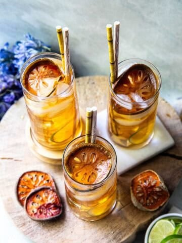 3 glasses for bael fruit juice on a cutting board with slices of bael fruit on the side.