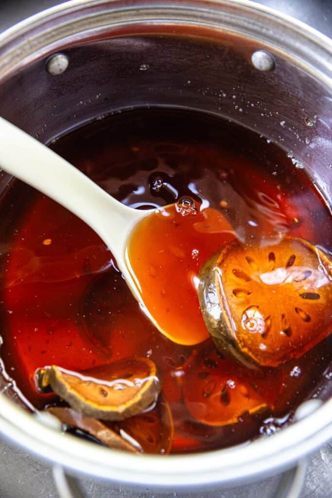 A ladle scooping up boiled bael slices in a pot of brown juice. 