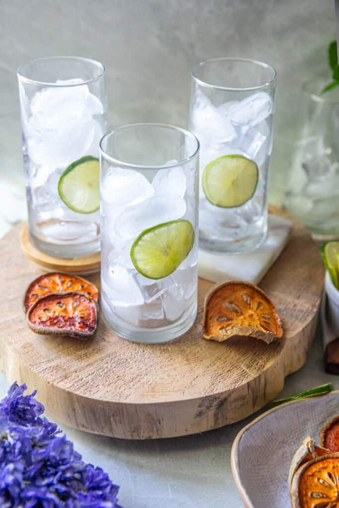 3 glasses filled with ice on top of a cutting board with beal fruit slices.  