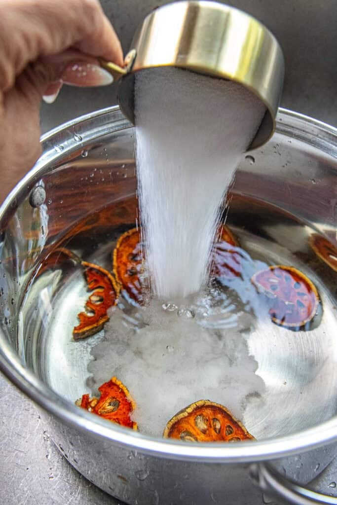 A measuring cup of sugar pouring into a pot of dried fruit slices. 