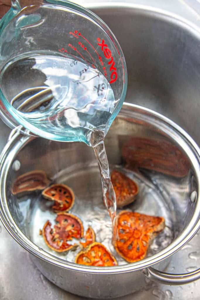 A glass of water pouring into a pot of dried fruit slices. 