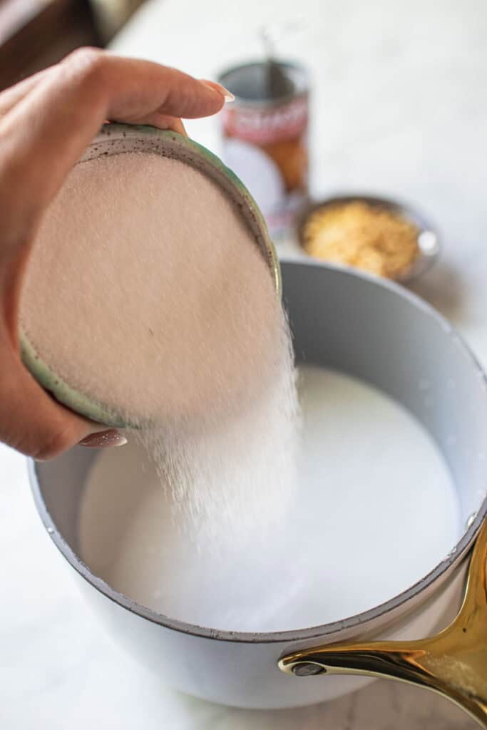 Sugar pouring into a pot of coconut cream. 
