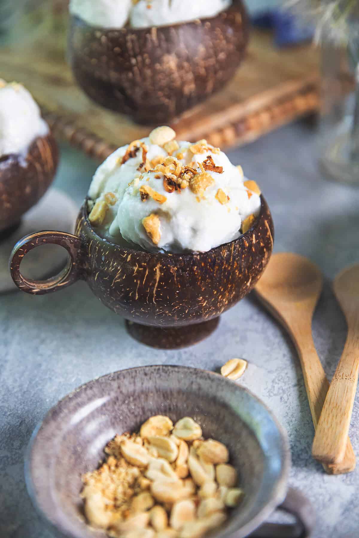 Thai coconut ice cream in a coconut bowl on a wooden tray on a table with crushed peanuts on top.