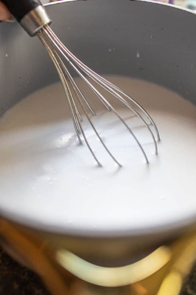 a whisk inside a pot of coconut cream. 