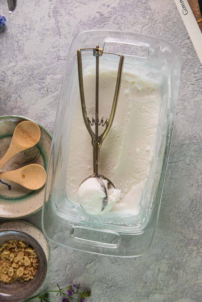 Ice cream scooper on top of a glass bowl with frozen coconut ice cream in the bottom. 