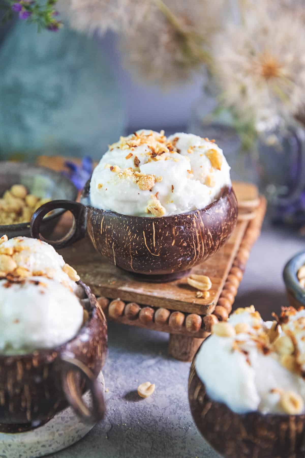 Thai coconut ice cream in coconut bowls on a wooden tray on a table with crushed peanuts. 