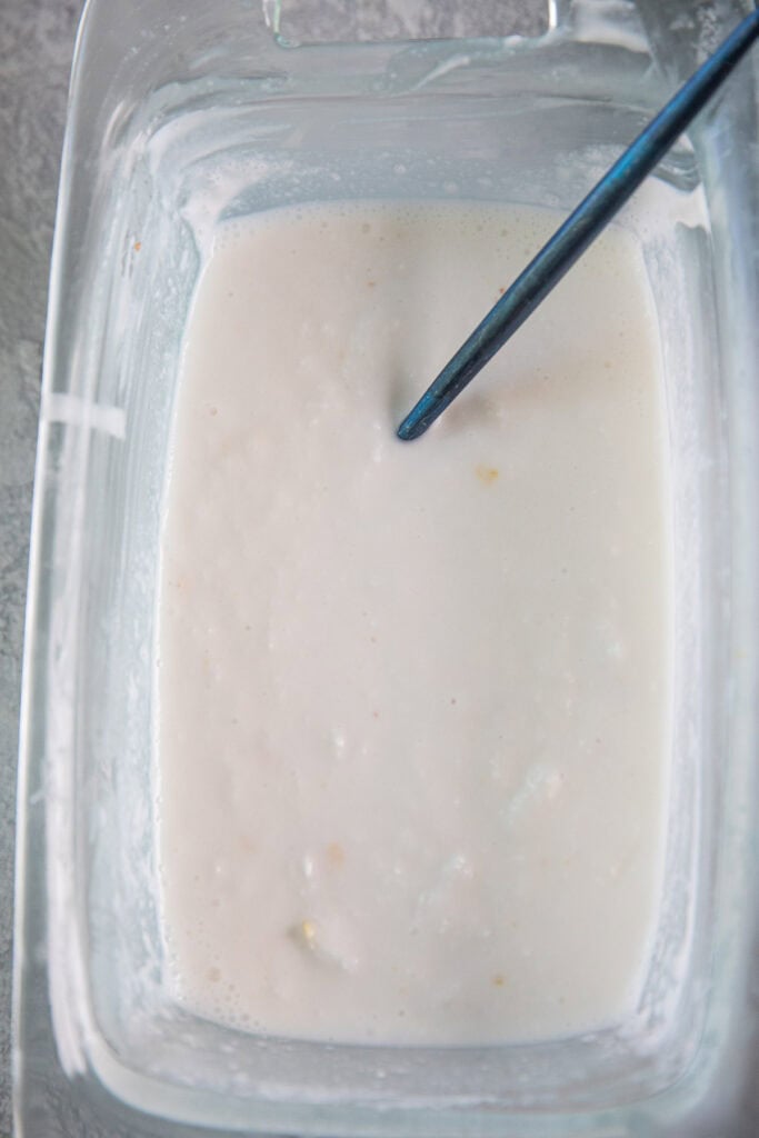 A spoon deep in a glass bowl of coconut ice cream mixture. 