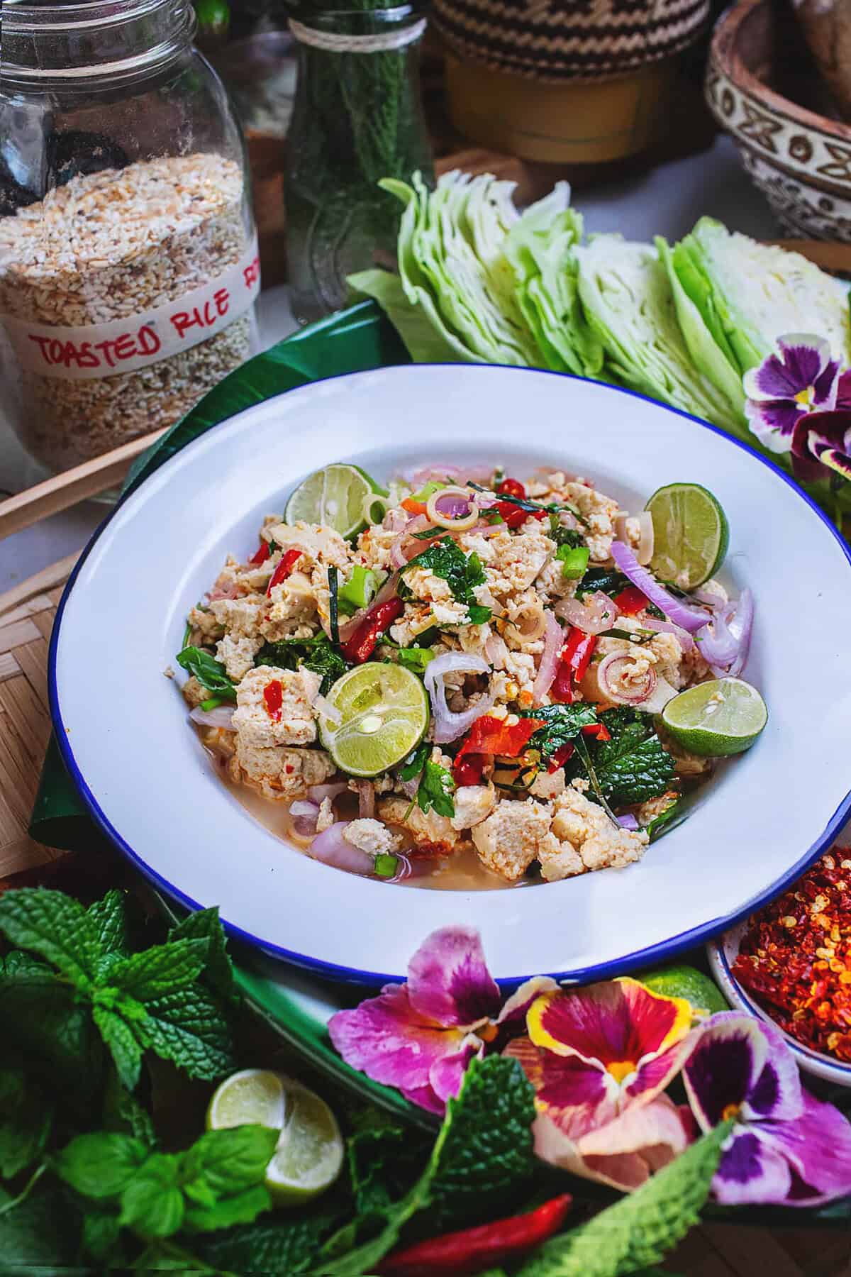 A plate of larb tofu on a tray with herbs and veggies on the side.