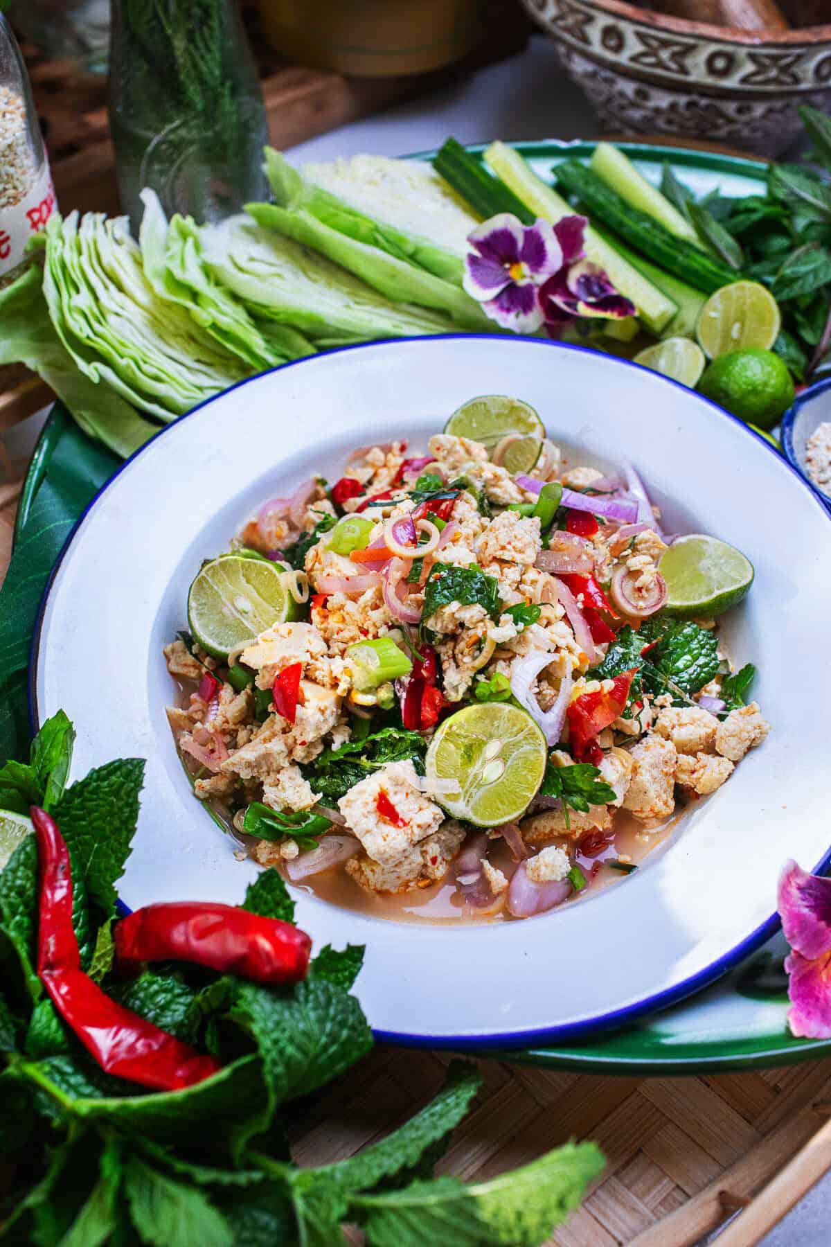 A plate of tofu larb on a tray with herbs and veggies on the side.  