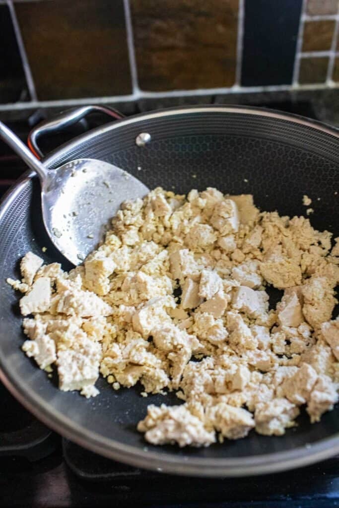 Crumbled tofu for vegan larb in a wok with a spatula.