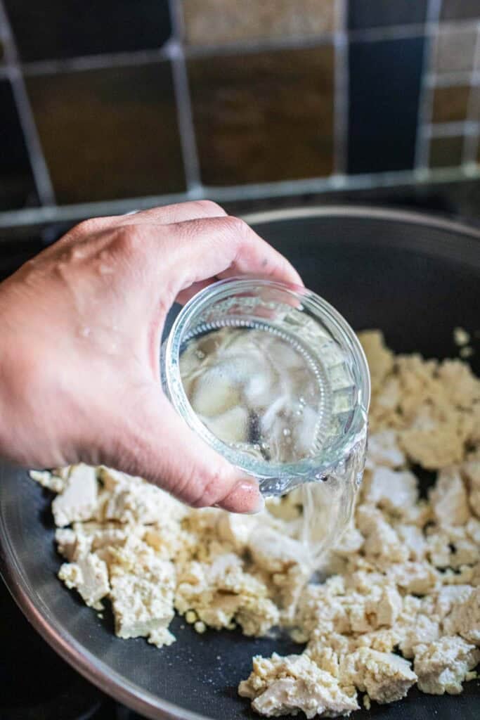 Water pouring into a wok of vegetarian larb crumbled tofu.
