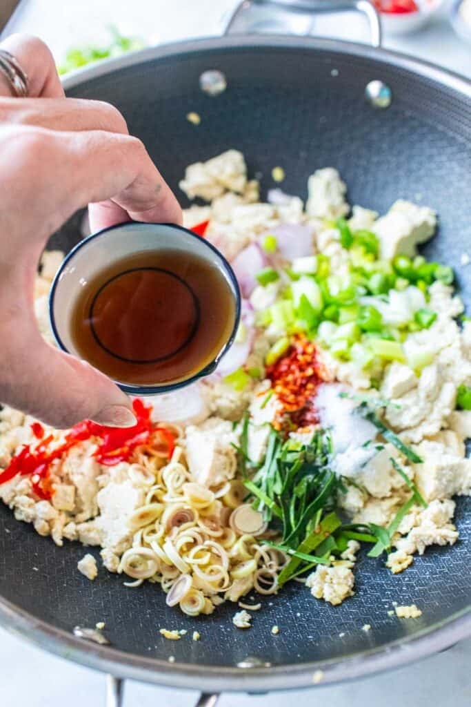 Fish sauce pouring into a wok of tofu larb salad. 