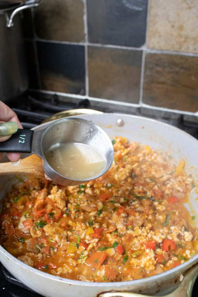 Stock pouring into a pan of tom yum meat mixture on a stove. 