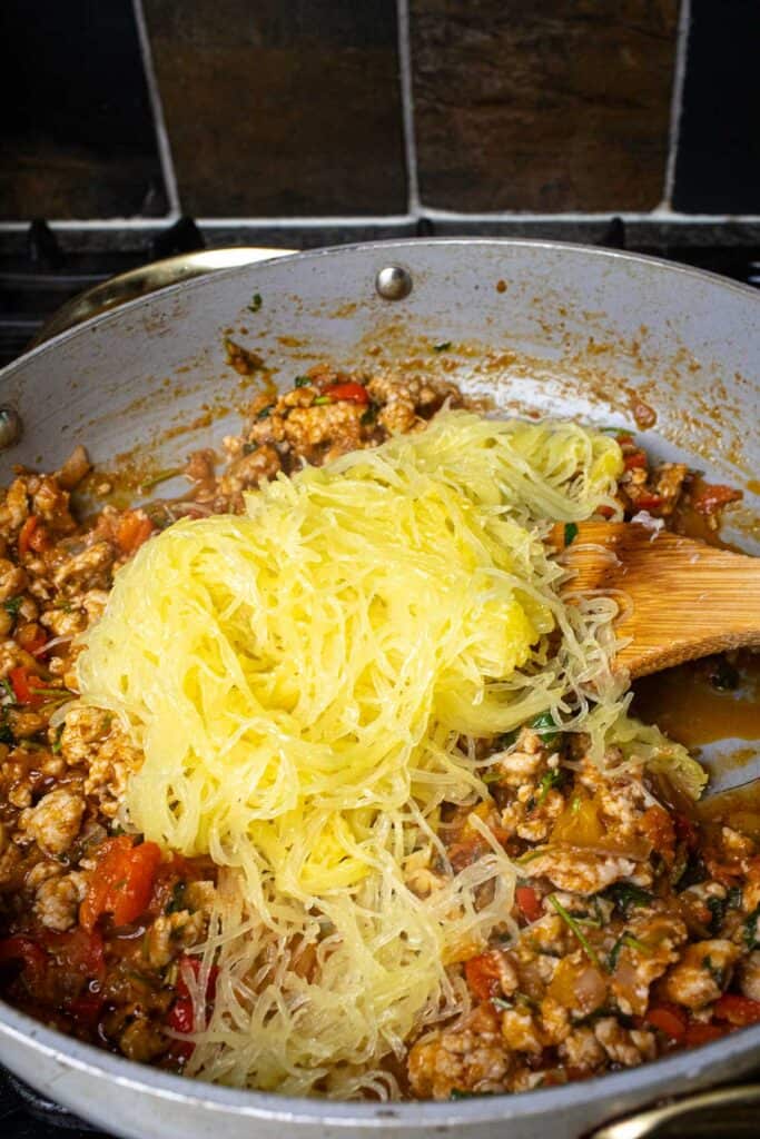 Shredded spaghetti squash on top of the tom yum meat mixture in a pan.