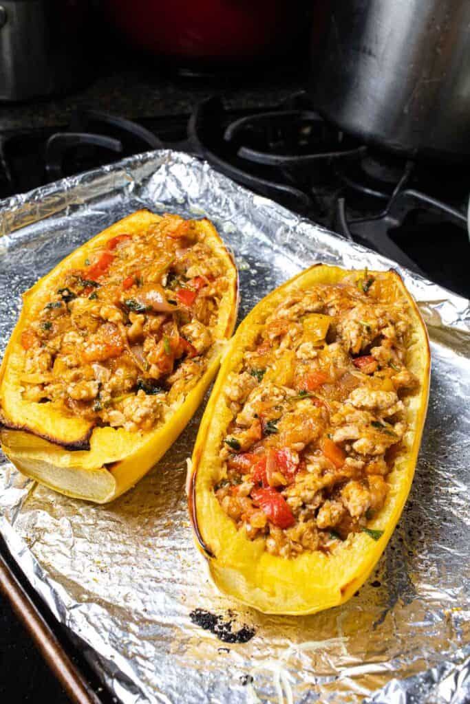 Two halves of a baked stuffed spaghetti squash with a meat mixture on top, on a baking sheet. 