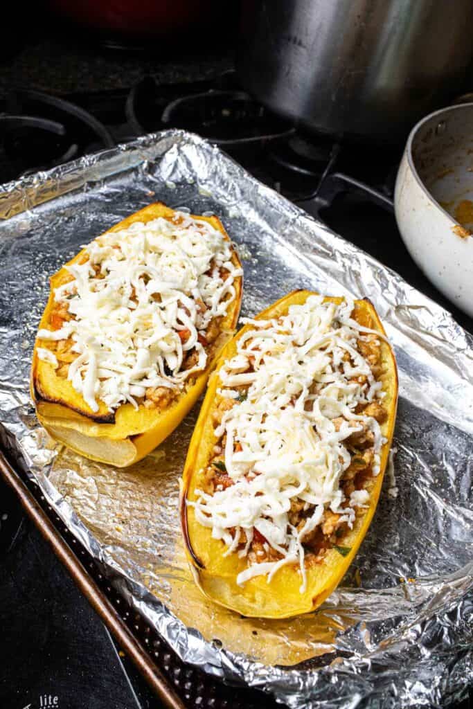 2 halves of baked stuffed spaghetti squash recipe with cheese on top on a baking sheet. 