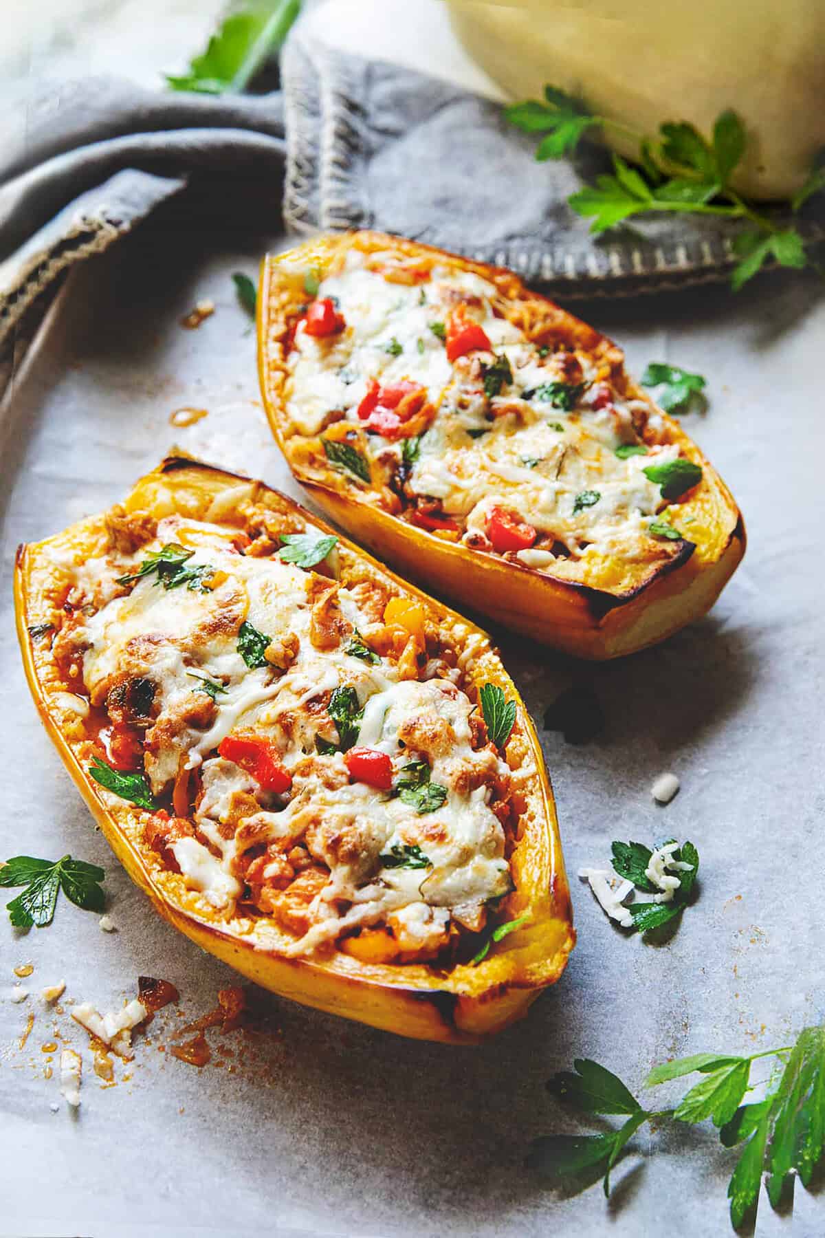 Two halves of baked stuffed spaghetti squash with melted cheese on top sitting on a baking sheet. 