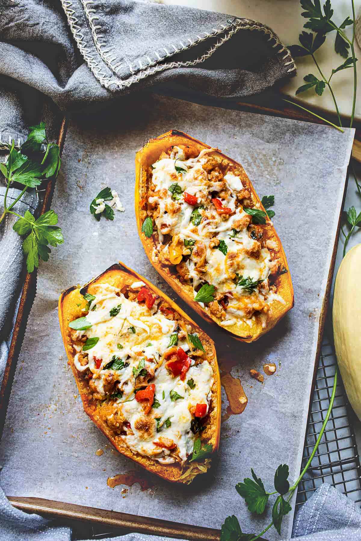 2 halves of baked stuffed spaghetti squash recipe with melted cheese on top on a baking sheet. 