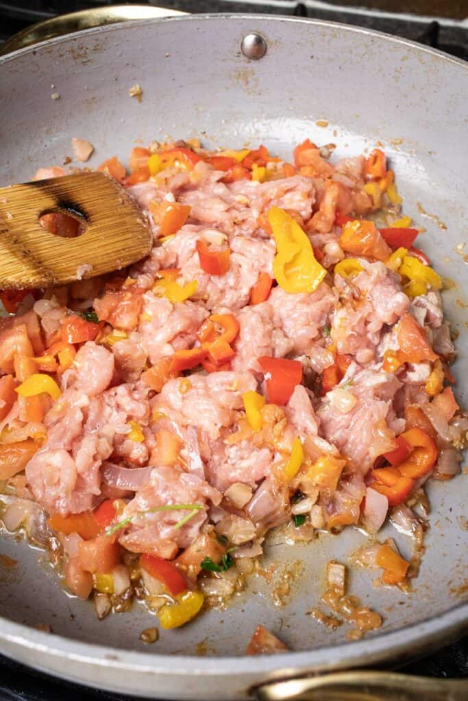 Ground meat and chopped pepper and onion in a pan on the stove. 