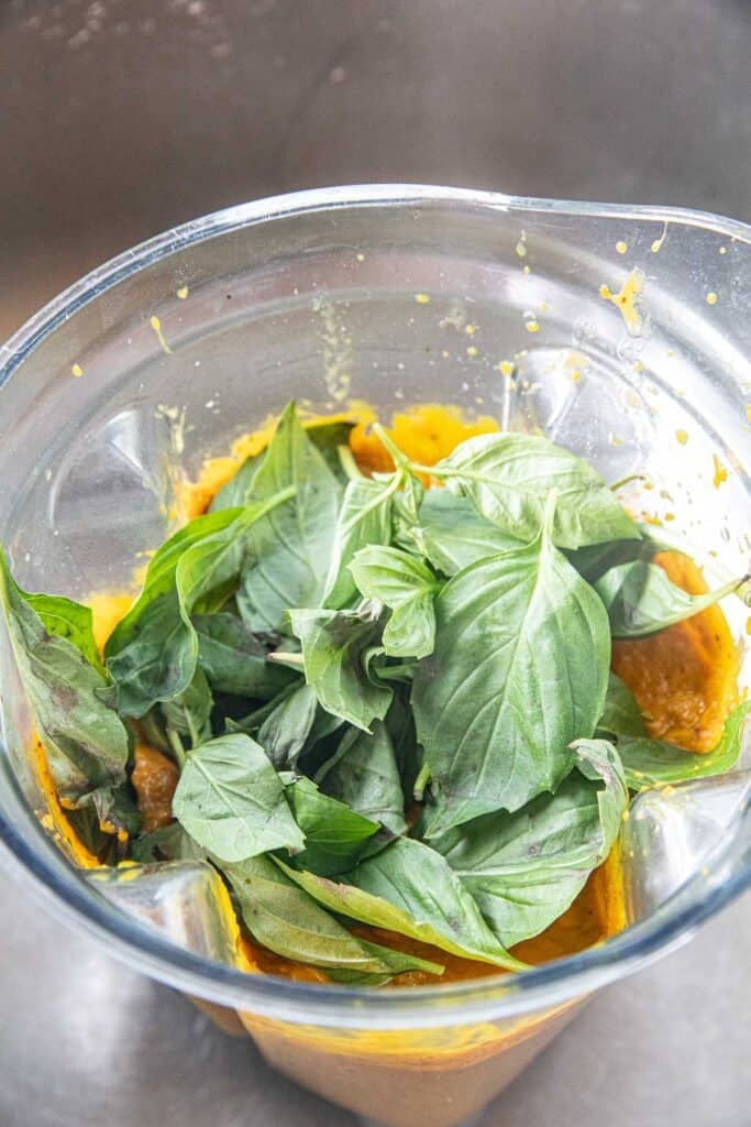 Basil leaves over a puree of pumpkin curry in a blender. 
