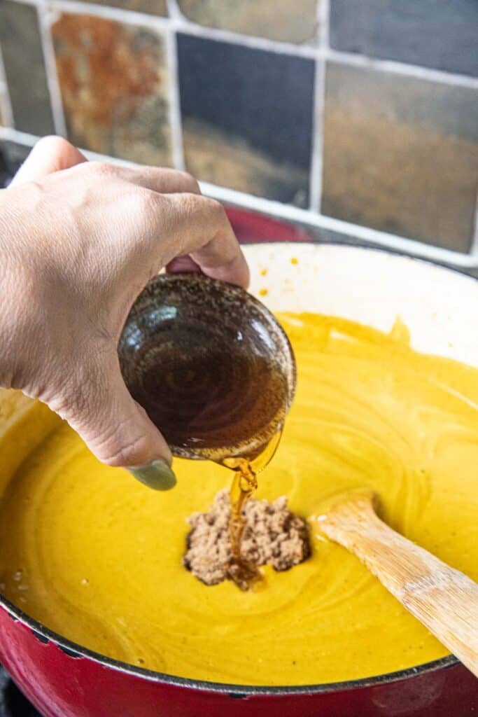 A hand pouring a small cup of fish sauce into a pot of Thai pumpkin curry. 
