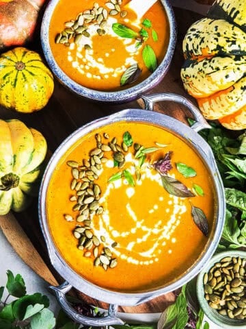 Two bowls of creamy Thai pumpkin curry on a table surrounded by pumpkins.