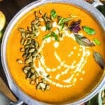 A bowl of creamy Thai pumpkin curry with pumpkin seeds and basil on a table.