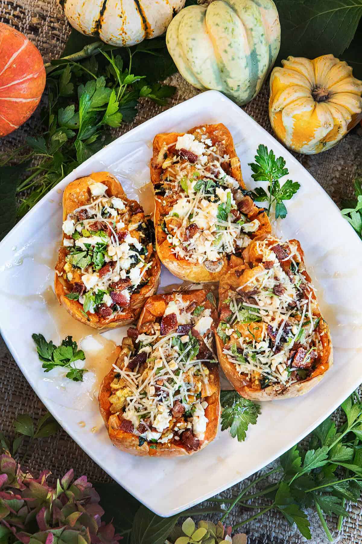 4 pieces of stuffed baked butternut squash on a tray with cheese and herb garnishes on a platter. t