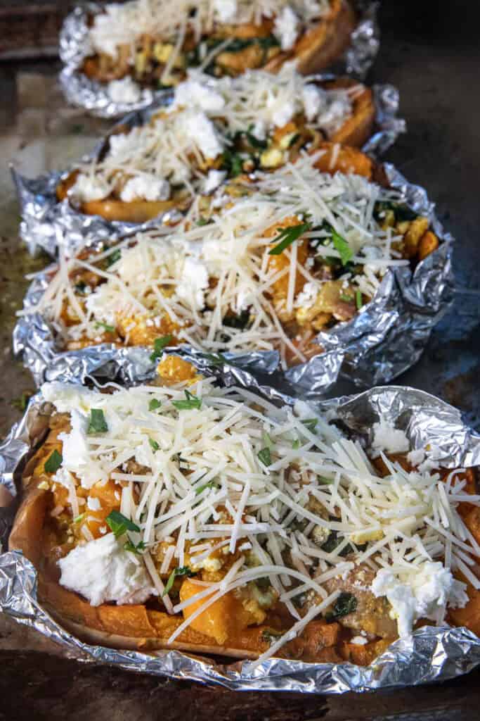 Roasted stuffed butternut squash halves topped with cheese and fresh herbs on a serving platter.