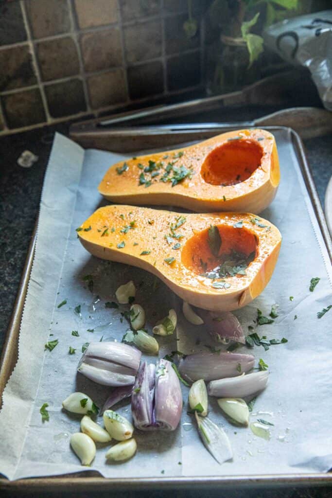 Halves butternut squash, shallot and garlic on a baking sheet.