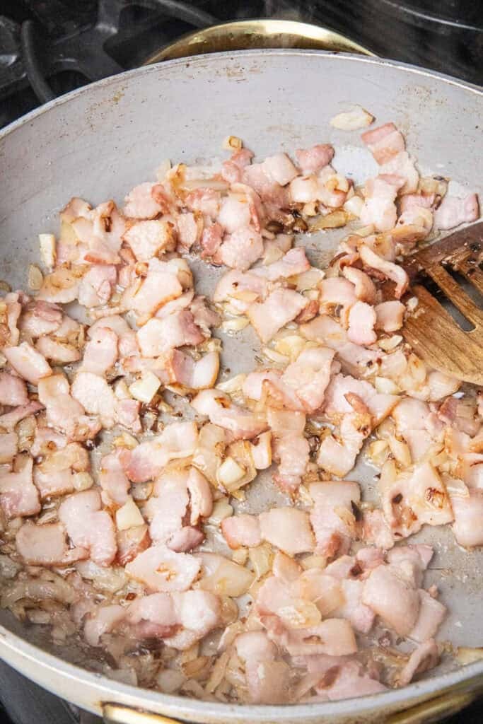 Sautéed bacon, garlic, and onion in a pan with a spatula. 