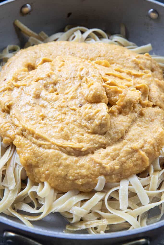 Blended butternut squash puree on top of pasta in acooking pan. 