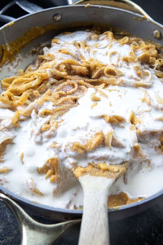 White cream on top of Blended butternut squash puree on top of pasta in acooking pan. 