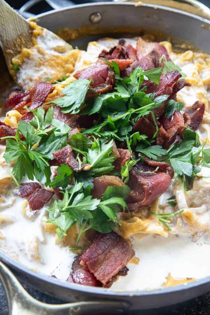 Bacon slices and parsley on top of White cream on top of pasta in a cooking pan. 