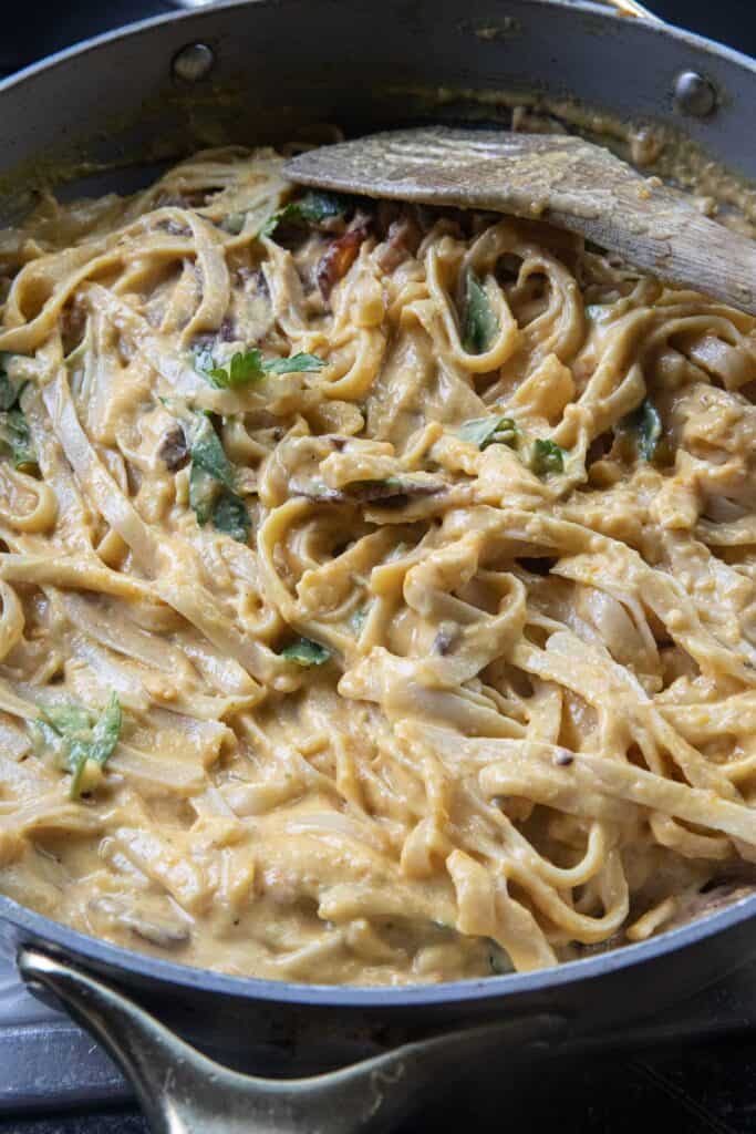 Creamy butternut squash pasta in a pan with a spatula on the side in a cooking pan. 