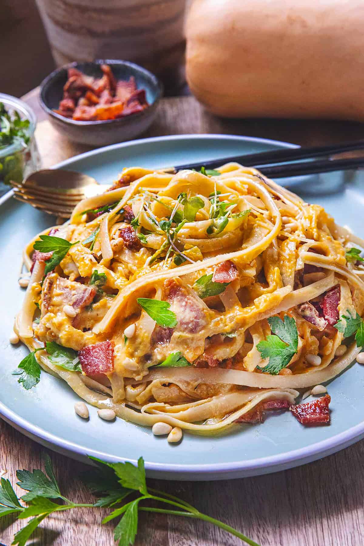 Creamy butternut squash pasta on a plate with green herb garnishes. 