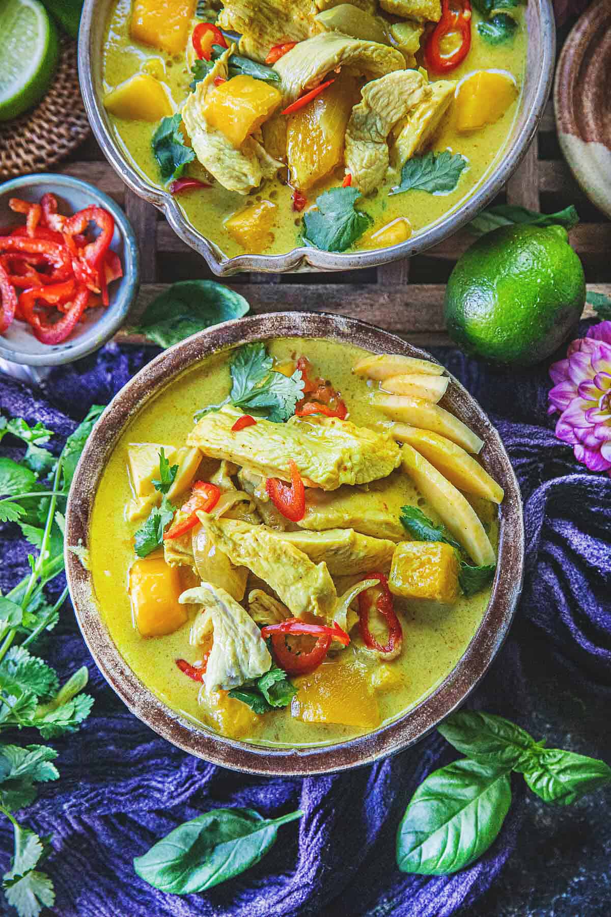 1 bowls of mango curry chicken surrounded by herbs and flowers. 