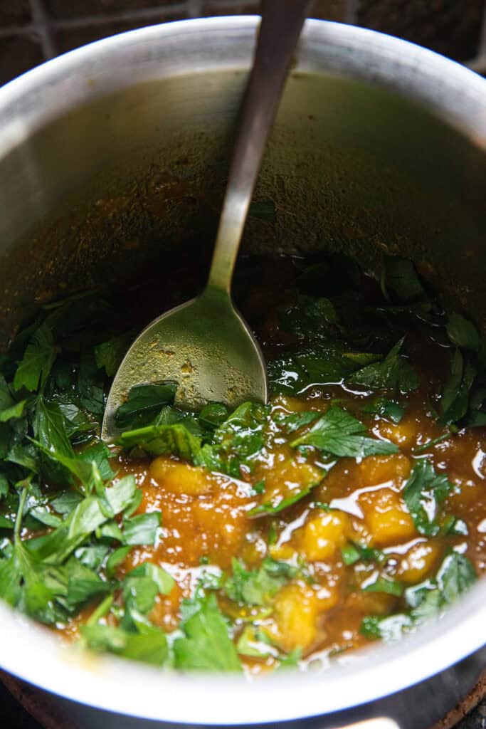 Cilantro over cooked yellow mixture for mango curry sauce in a pot with a spoon in the middle.