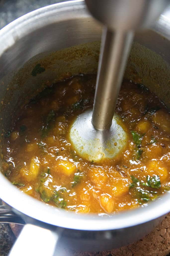 Immersion blender in a  cooked yellow mixture for mango curry sauce in a pot. 