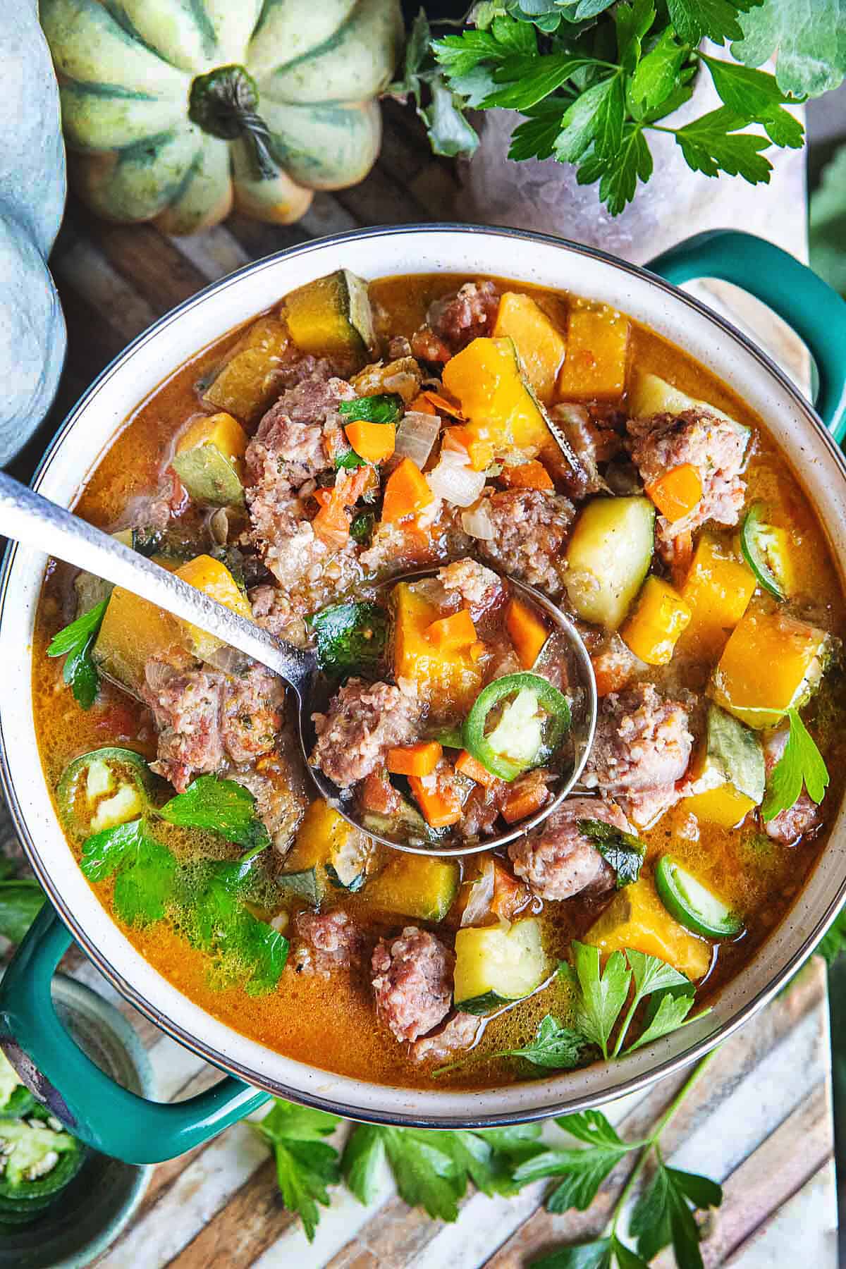 Thai pumpkin soup in a small pot with a ladle in the middle and garnishes around it. 