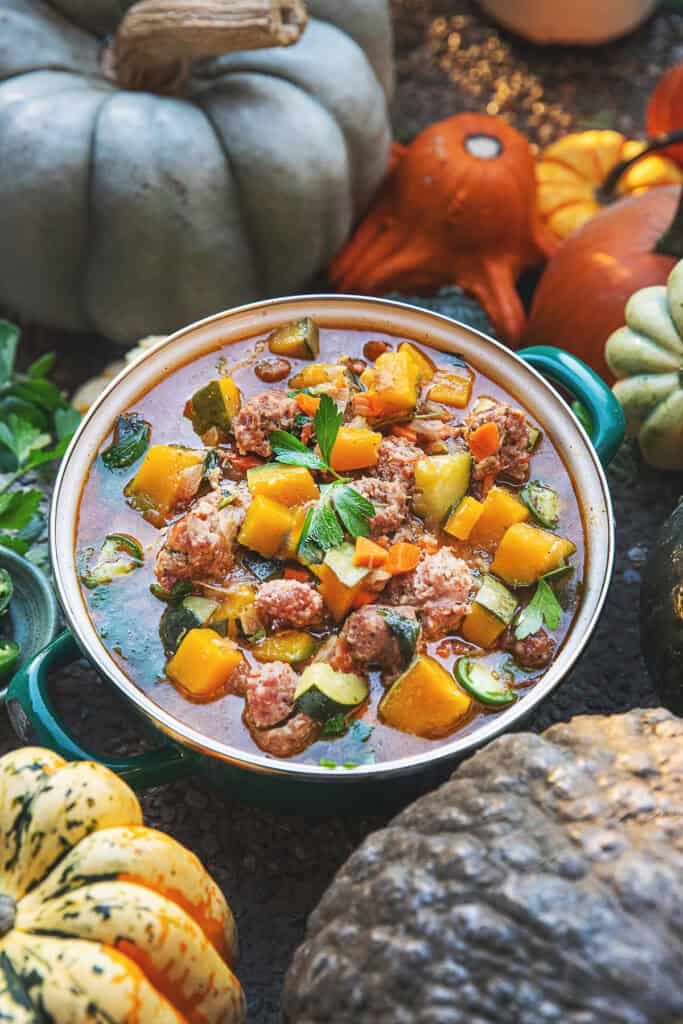 Thai pumpkin soup in a small pot and pumpkins, squashed and garnishes around it. 