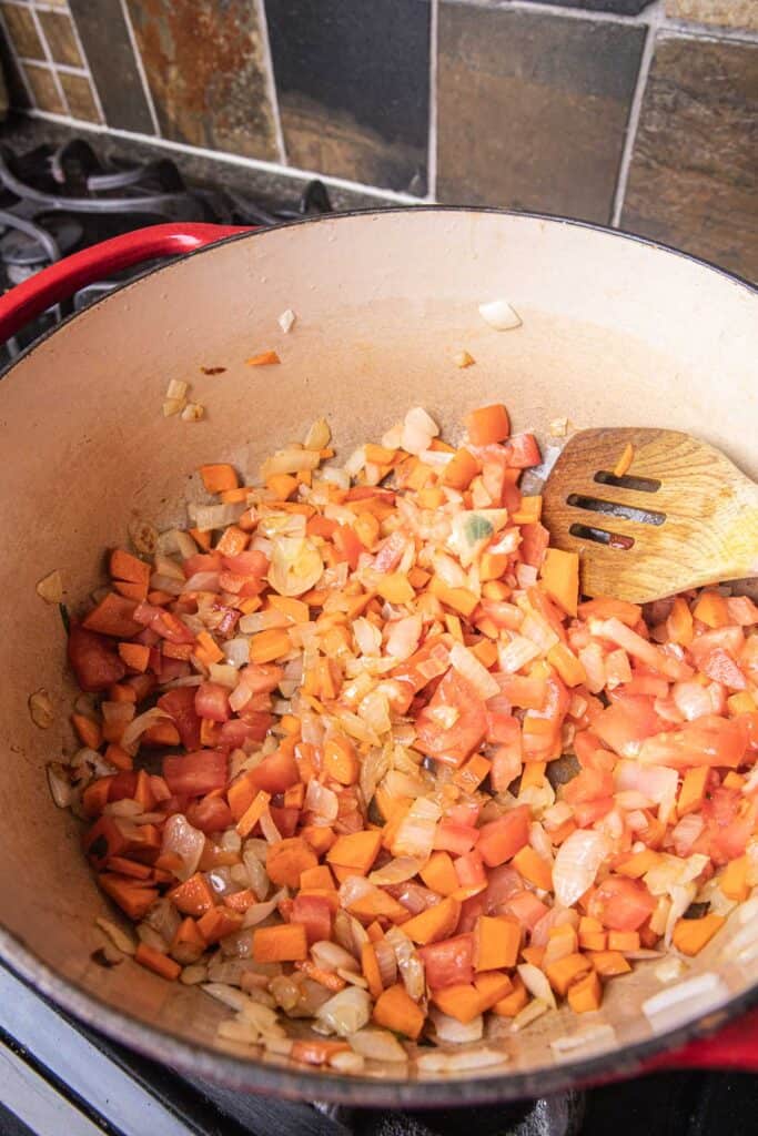 Sauteed onion, garlic, carrot and tomato in a pot on the stove. 