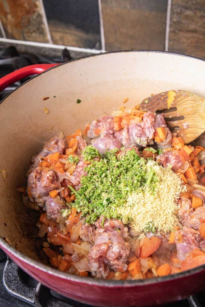 Sauteed sausage with onion, garlic, carrot and tomato in a pot on the stove. 