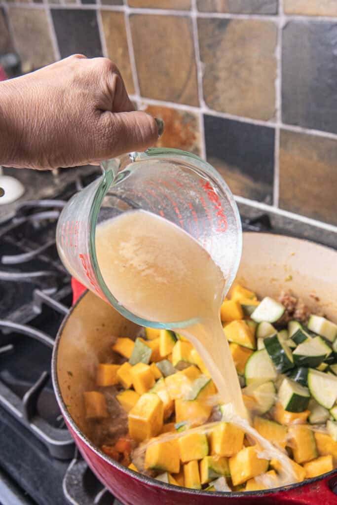 Stock pouring into a pot of chopped pumkin on the stove. 