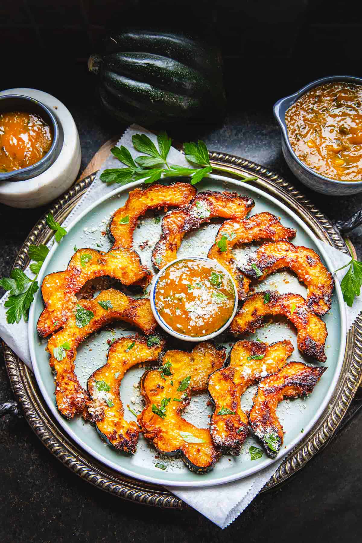 Roasted acorn squash slices on a plate with mango curry sauce in a small bowl in the middle. 