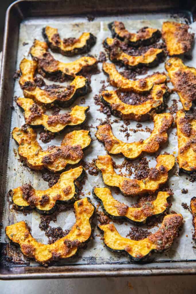 Roasted Acorn squash slices with tom yum paste coating on a lined baking pan. 