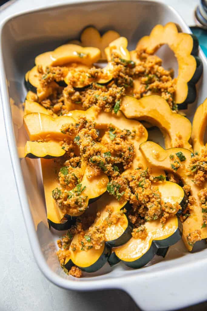 Acorn squash slices with tom yum paste coating in a baking dish.