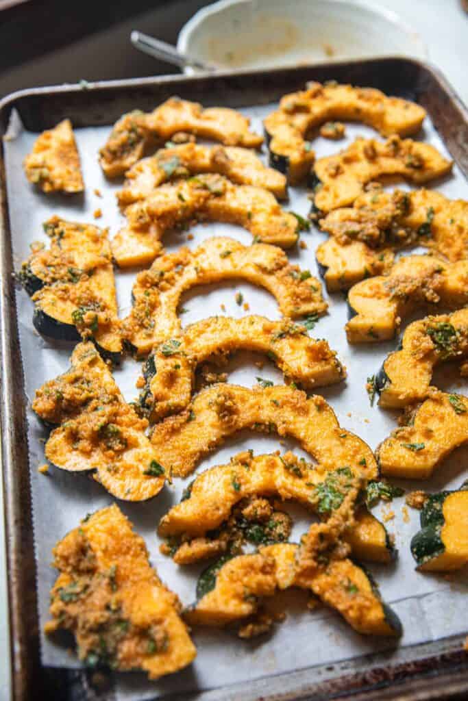 Acorn squash slices with tom yum paste coating on a lined baking pan. 