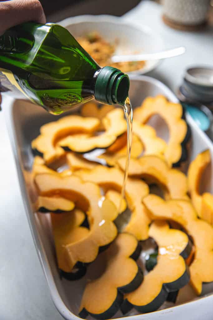 Oil pouring from a bottle into sliced acorn squash in a baking pan. 